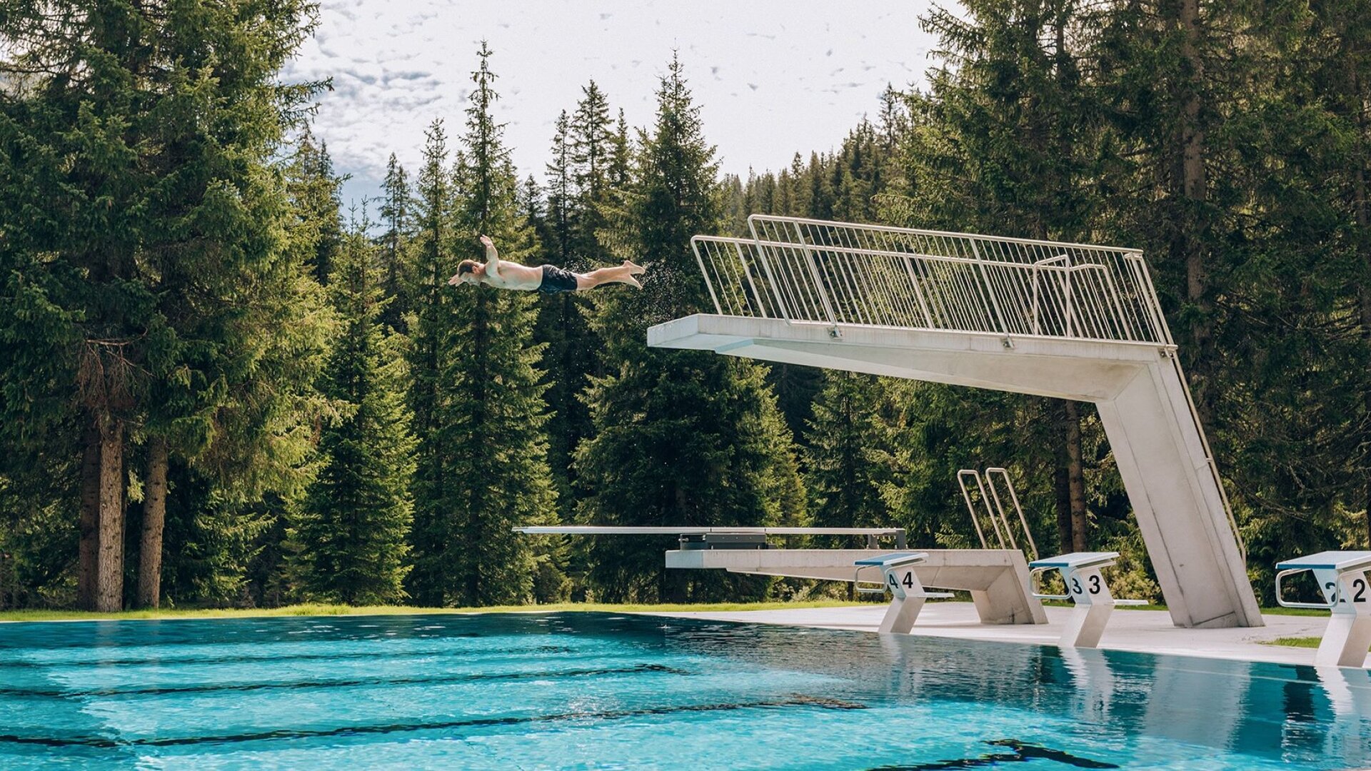Mann springt vom Sprungturm ins Schwimmbecken